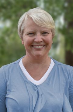 En leende person i ljusblå topp mot en suddig bakgrund av grönska.