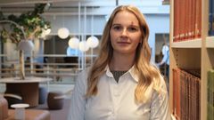 Bild på en kvinna som står vid en bokhylla på ett universitet.