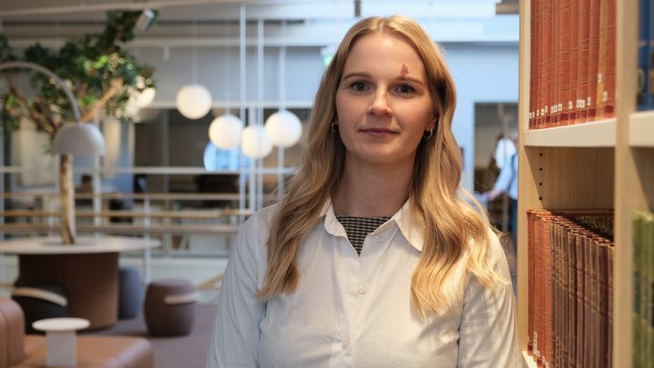 Bild på en kvinna som står vid en bokhylla på ett universitet.