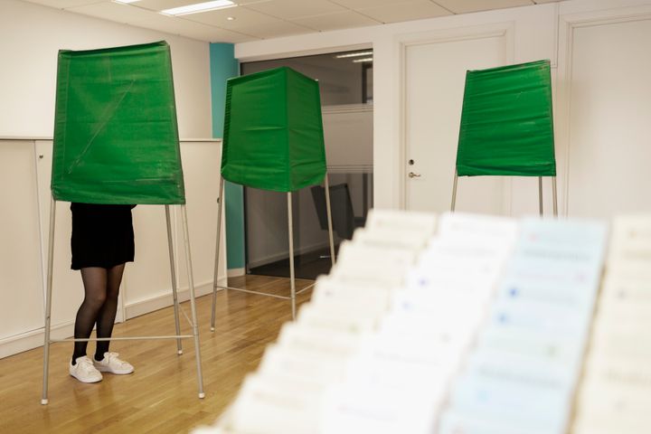 Tre röstbås i en svensk vallokal, en person står i ett av båsen.
