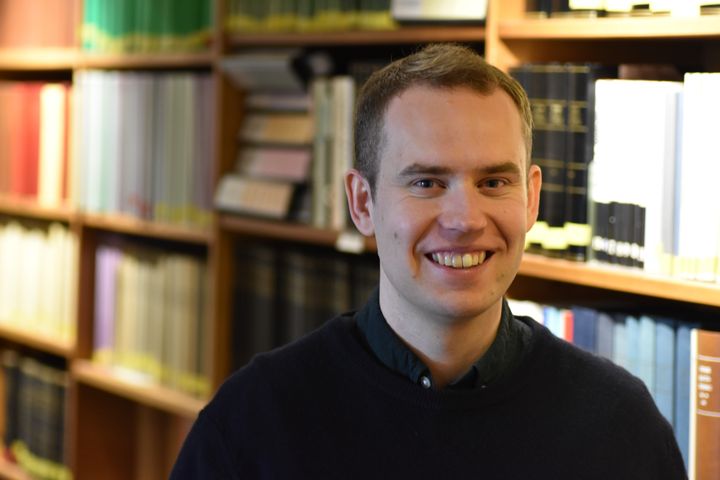 En person i en biblioteksmiljö, omgiven av böcker.