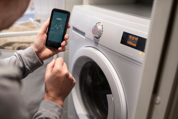 En person håller en smartphone framför en tvättmaskin.