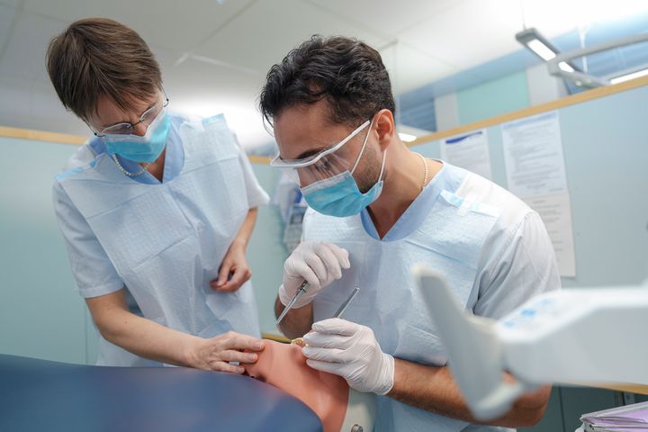 Två studenter med munskydd tittar i patientmun