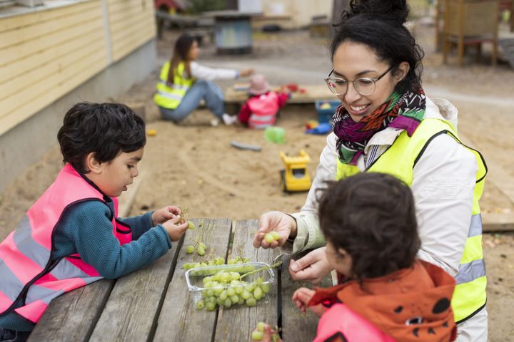 Förskolepedagog med två barn utomhus.