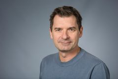 Porträtt av en man i en blå tröja mot en grå bakgrund.