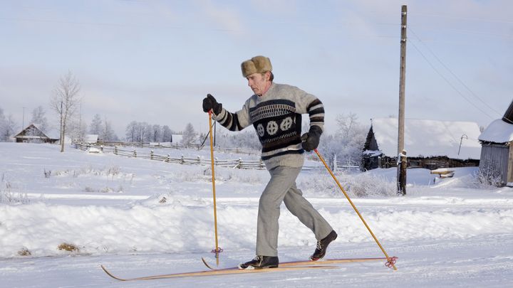 En person åker längdskidor i ett vinterlandskap med snö, iklädd en varm tröja och pälsmössa.