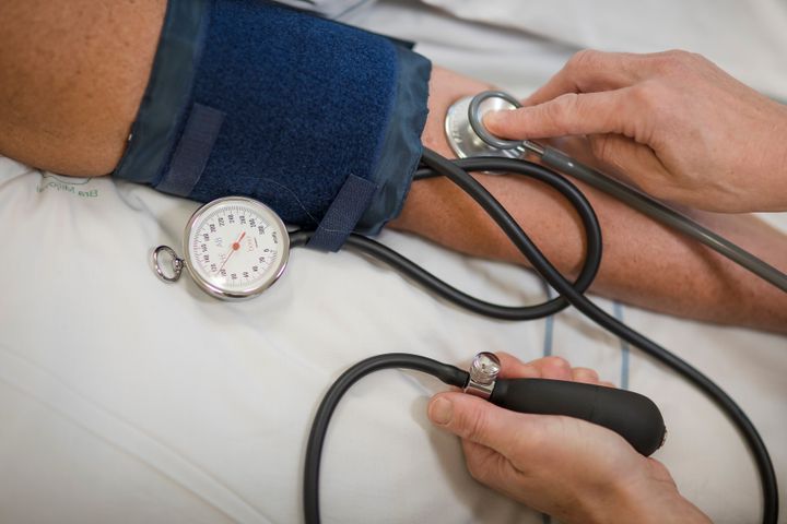 Vårdpersonal mäter blodtrycket på en patients arm med manschett och stetoskop.