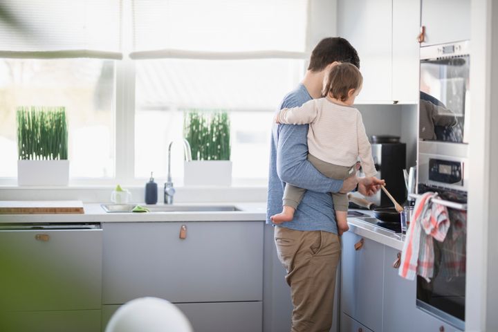 Förälder håller ett spädbarn i köket medan hen lagar mat.