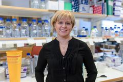 A person standing in a laboratory with shelves of bottles and containers in the background.