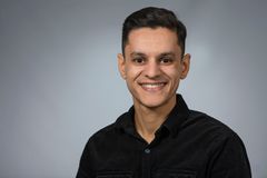 Person smiling, wearing a black shirt against a gray background.