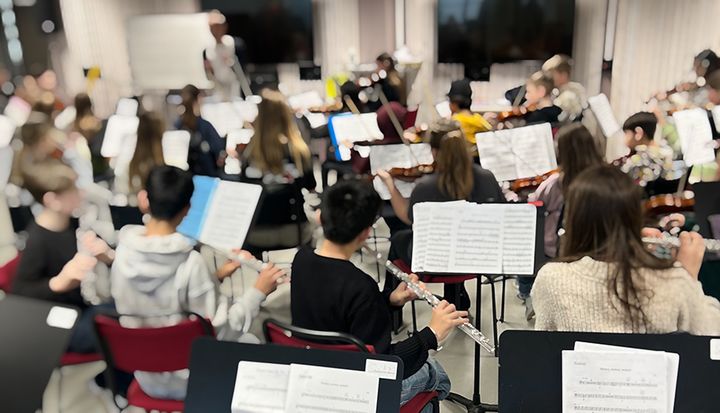 En grupp ungdomar spelar olika musikinstrument i ett orkesterrum.