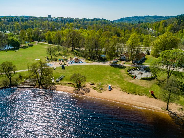 Flygfoto av en badplats i Borås med en strand, lekpark och grönska.