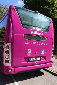 Rosa buss med texten "Valbuss Här kan du rösta", parkerad på en gata.