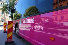 En rosa valbuss med texten "Valbuss här kan du rösta" parkerad vid en kyrka.