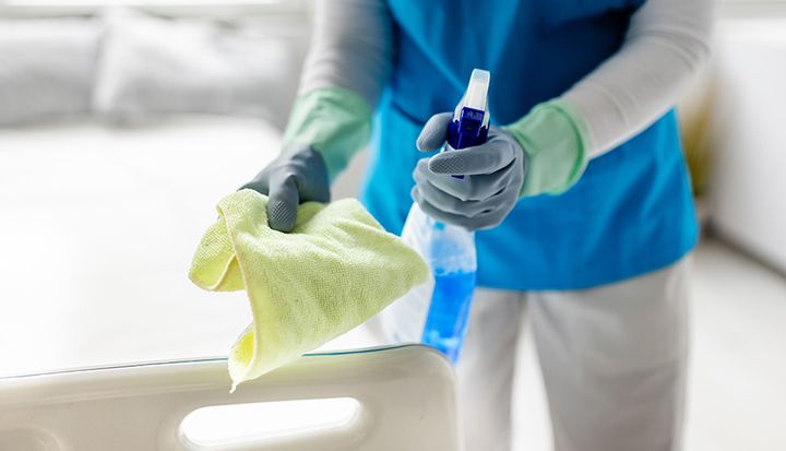 Städpersonal med handskar på händerna håller i en trasa och en sprejflaska