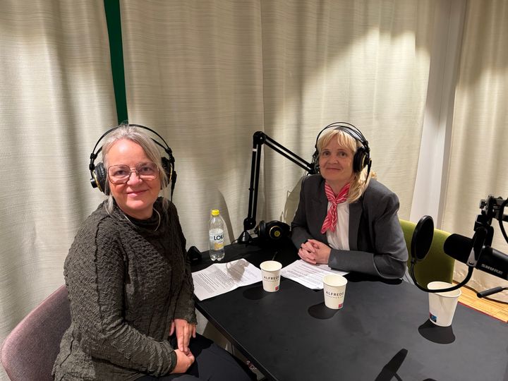 Två kvinnor sitter vid ett bord med mikrofoner och hörlurar i en inspelningsstudio.