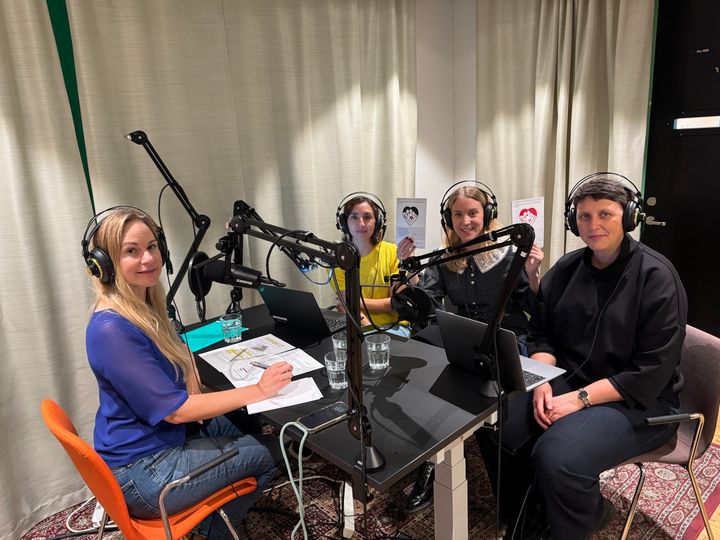 Fyra personer sitter vid ett bord med mikrofoner och hörlurar, deltar i en inspelning eller intervju i en studio.