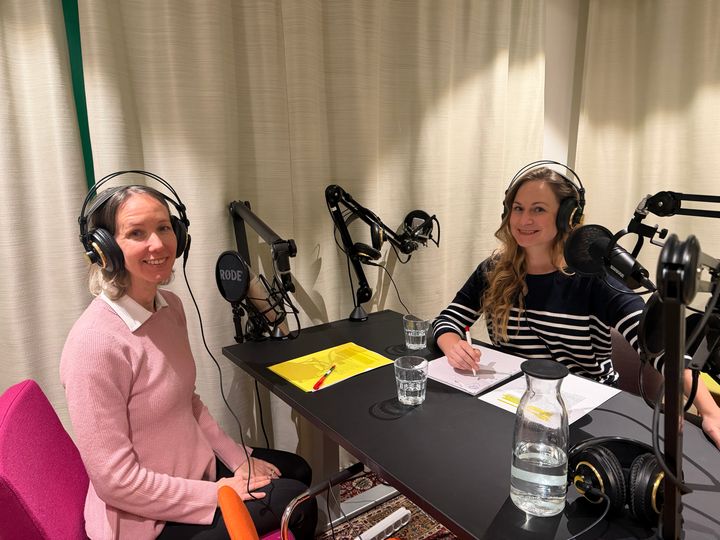 Två personer sitter vid ett bord i en radiostudio med mikrofoner och hörlurar.