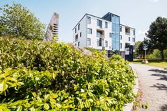 Ljust flerfamiljshus med grönska i förgrunden under klar himmel.