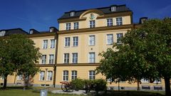 Stor gul putsad hyresfastighet med träd och två kanoner framför.