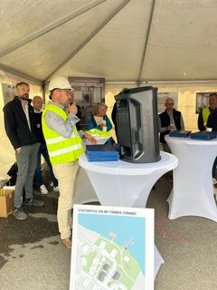 Per Morelius från HSB Södermanland iförd bygghjällm och väst talar inför de närvarande under ett tält.