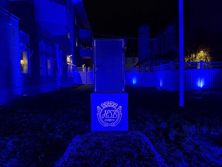 Ljusinstallation i mörkblått. En dörr på ett podie med HSB Norrs logga som strålar med varmt ljus