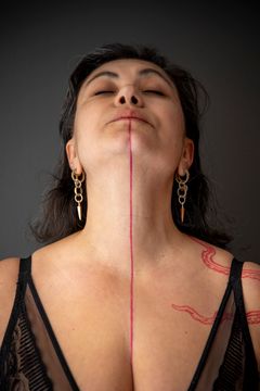 Elcim "Superturken” Yilmaz blundar och tittar upp mot taket. vi ser hennes tatuerade linje från munnen som fortsätter neråt samt en röd tatuering på axeln