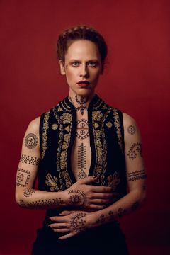 Eva Balazin fotograferad mot röd bakgrund och visar traditionsenliga motiv på kroppen
