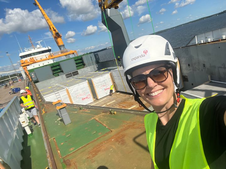 Henkil%F6%20suojavarusteissa%20laivan%20kannella%2C%20taustalla%20nosturi%20ja%20kuljetettavia%20moduulirakenteita.