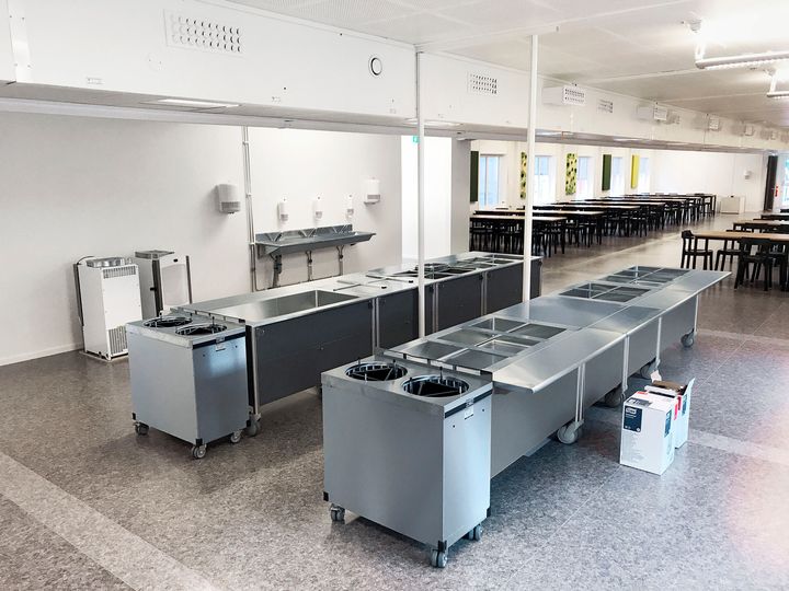 Suuri%20ruokala-%20ja%20linjastotila%20moduulirakennuksen%20sis%E4ll%E4.%20Kuvassa%20n%E4kyy%20tarjoilulinjastoja%2C%20ruokap%F6yti%E4%20sek%E4%20avara%20ruokailutila%2C%20jossa%20on%20valkoiset%20sein%E4pinnat%20ja%20teollisuustyyppinen%20valaistus.