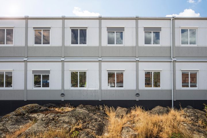 Kaksikerroksisen%20moduulirakennuksen%20julkisivu%20kallioisessa%20ymp%E4rist%F6ss%E4.%20Kuvassa%20n%E4kyy%20vaaleas%E4vyinen%20rakennus%20riveitt%E4in%20sijoitettuine%20ikkunoineen%20sek%E4%20rakennuksen%20edustalla%20luonnonkalliota%20ja%20kuivaa%20heinikkoa.
