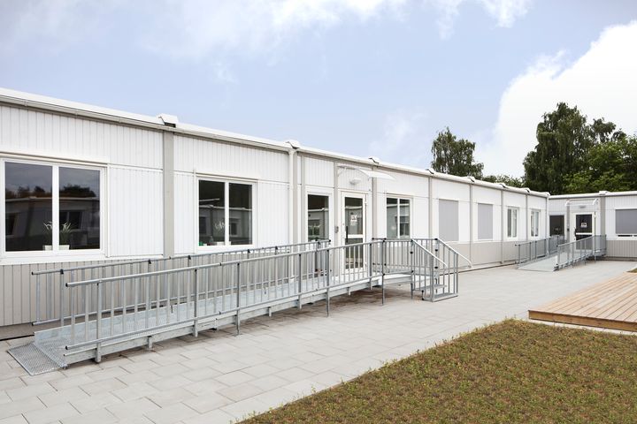 Yksikerroksinen%20moduulirakennus%20esteett%F6mill%E4%20kulkureiteill%E4%20ja%20loivilla%20luiskilla%20varustettuna.%20Kuvassa%20n%E4kyy%20vaalea%20rakennuskokonaisuus%2C%20piha-alue%20sek%E4%20metalliset%20kaiteet%20rakennuksen%20sis%E4%E4nk%E4yntien%20edustalla.