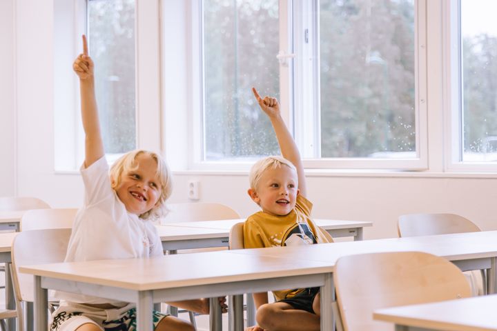 Kaksi%20oppilasta%20istuu%20luokkahuoneessa%20k%E4det%20pystyss%E4%20valmiina%20vastaamaan%20opettajan%20kysymykseen.%20Valoisa%20oppimisymp%E4rist%F6%20ja%20suuret%20ikkunat%20luovat%20viihtyis%E4t%20puitteet%20koulup%E4iv%E4%E4n.