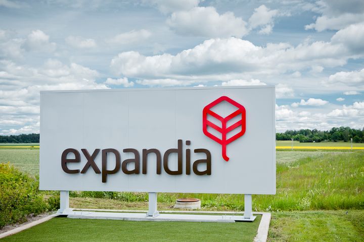 Expandian%20logo%20ja%20yrityskyltti%20avoimen%20peltomaiseman%20laidalla.%20Yrityksen%20tunnus%20n%E4kyy%20valkoisella%20taustalla%20pilvisen%20taivaan%20alla.