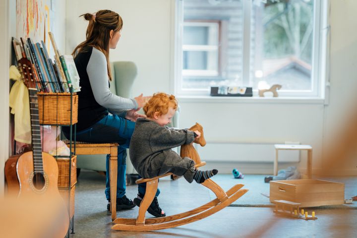 Valoisa%20tila%2C%20edustalla%20lapsi%2C%20joka%20keinuu%20keinuhevosella.%20Taaempana%20nainen%2C%20joka%20katsoo%20kohti%20ikkunaa.