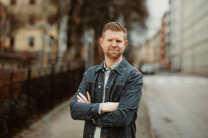 Man med kort hår och jeansjacka. Han står utomhus med armarna i kors.