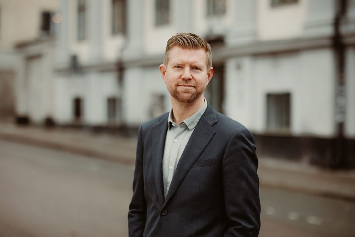 Man med kort hår, står utomhus, iklädd skjorta och kavaj.
