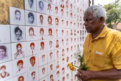Brito Fernando står framför en vägg med porträtt på personer som har försvunnit. Han håller i blommor.