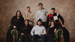 En grupp unga människor sitter och står kring en soffa, alla ler mot kameran.