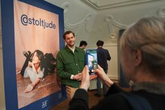 En ung man blir fotograferad vid utställningen @stoltjude, där en stor affisch syns i bakgrunden.