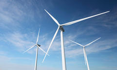 Tre vindkraftverk under en klar blå himmel.