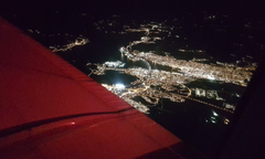 Flygfoto över en stad nattetid, tagen från ett flygplan. Stadens ljus syns tydligt mot mörkret.