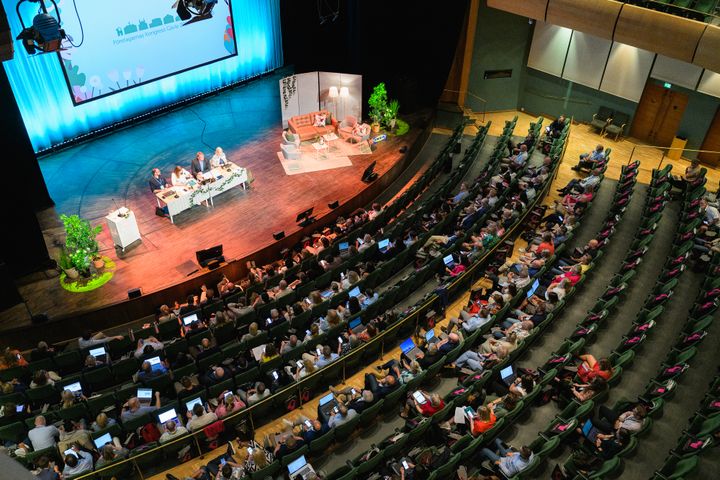 En välfylld konferenssal med en presentation på scenen.