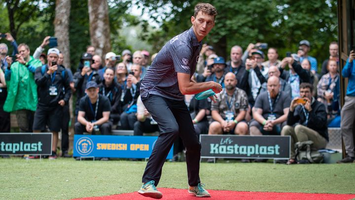 En person kastar en disc på en frisbee-tävling, med publik i bakgrunden.