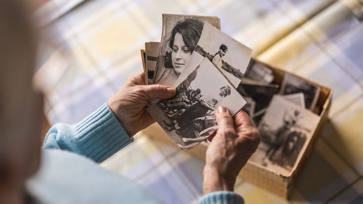 Person som håller i gamla fotografier ovanför en låda, på ett rutigt tygunderlag.