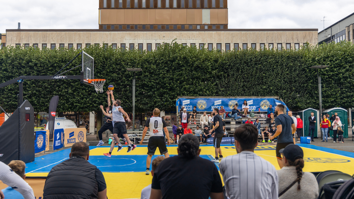 En grupp män spelar basket på en utomhusplan inför åskådare.
