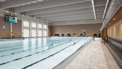 Alt text: Inomhuspool med simmare och läktare vid sidan av bassängen.