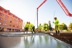 Byggarbetare i gula skyddskläder gjuter en betongplatta vid byggplatsen för det nya kommunhuset i Huddinge.