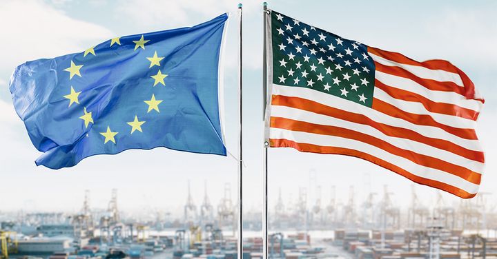 Alt text: EU-flagga och USA-flagga vajande på flaggstänger med en hamn i bakgrunden.