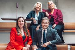 Bild på fyra personer som sitter och står runt en bänk, leende och klädda i affärskläder.